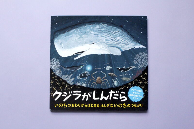 クジラが描かれた絵本の表紙で、深海の様子や生き物たちが描かれている。タイトルは「クジラがしんだら」で、夜空の中にクジラのイラストがある。